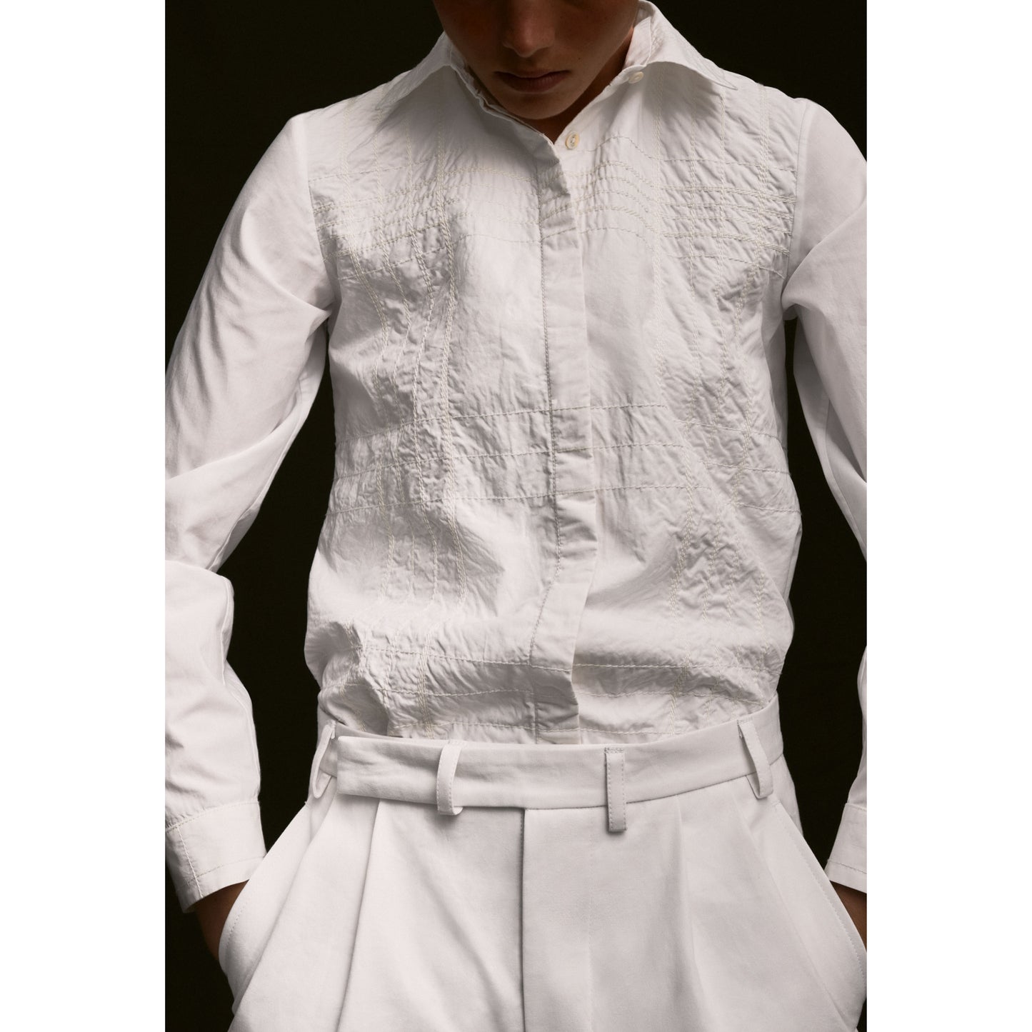 Person wearing a white textured shirt and pants with a black background